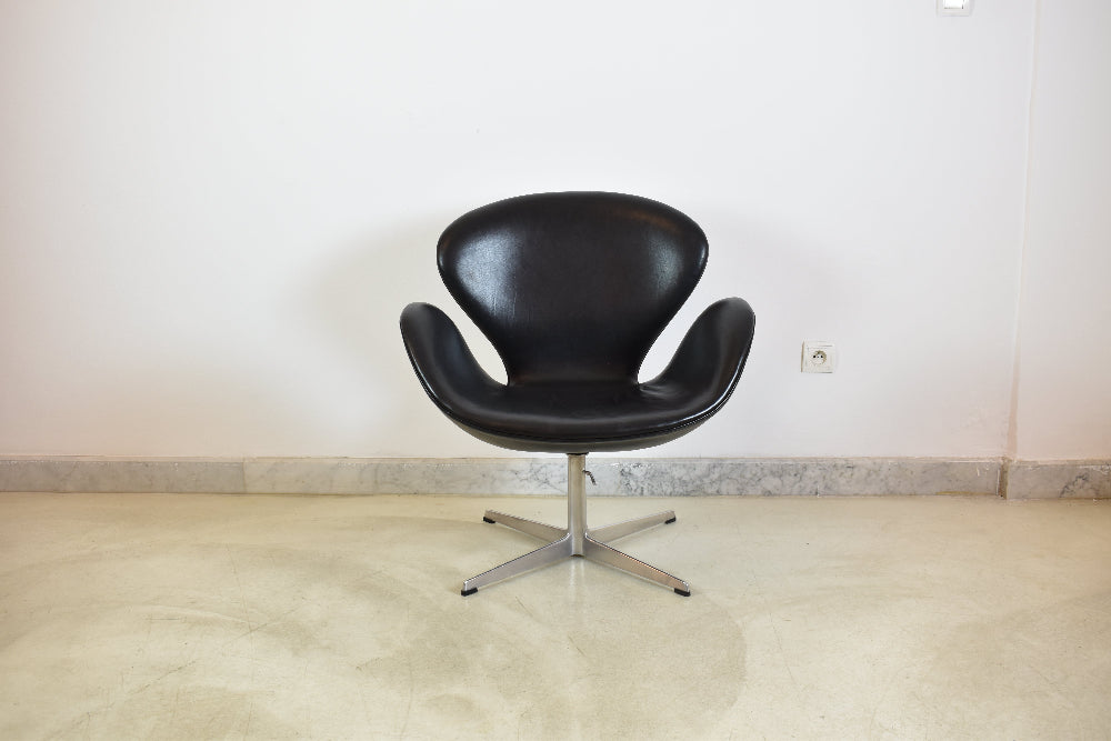 Front view of a restored black leather Fritz Hansen Swan armchair on a light tile floor against a white wall.

