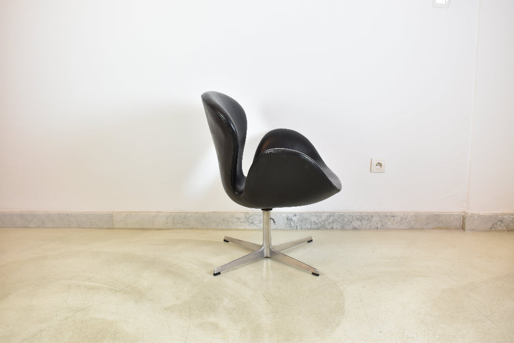 Side profile view of a mid-century modern black leather Swan chair on a 4-star aluminum swivel base.
