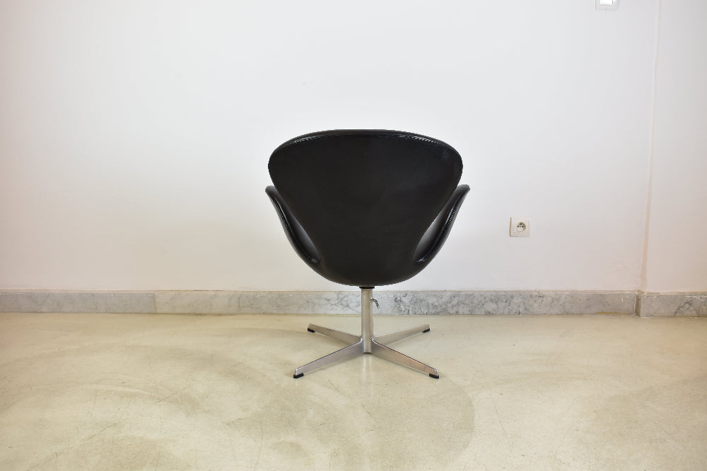 Back view of a minimalist black leather accent chair, showcasing its smooth organic shell structure.
